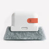 A white groove cleaning brush with an orange scouring head resting on a gray foam surface.