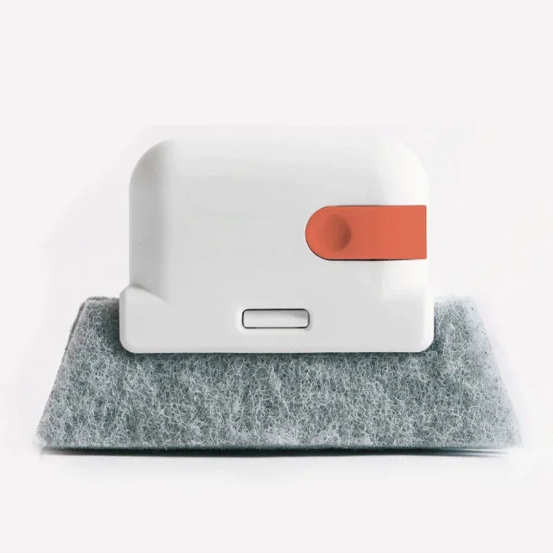 A white groove cleaning brush with an orange scouring head resting on a gray foam surface.