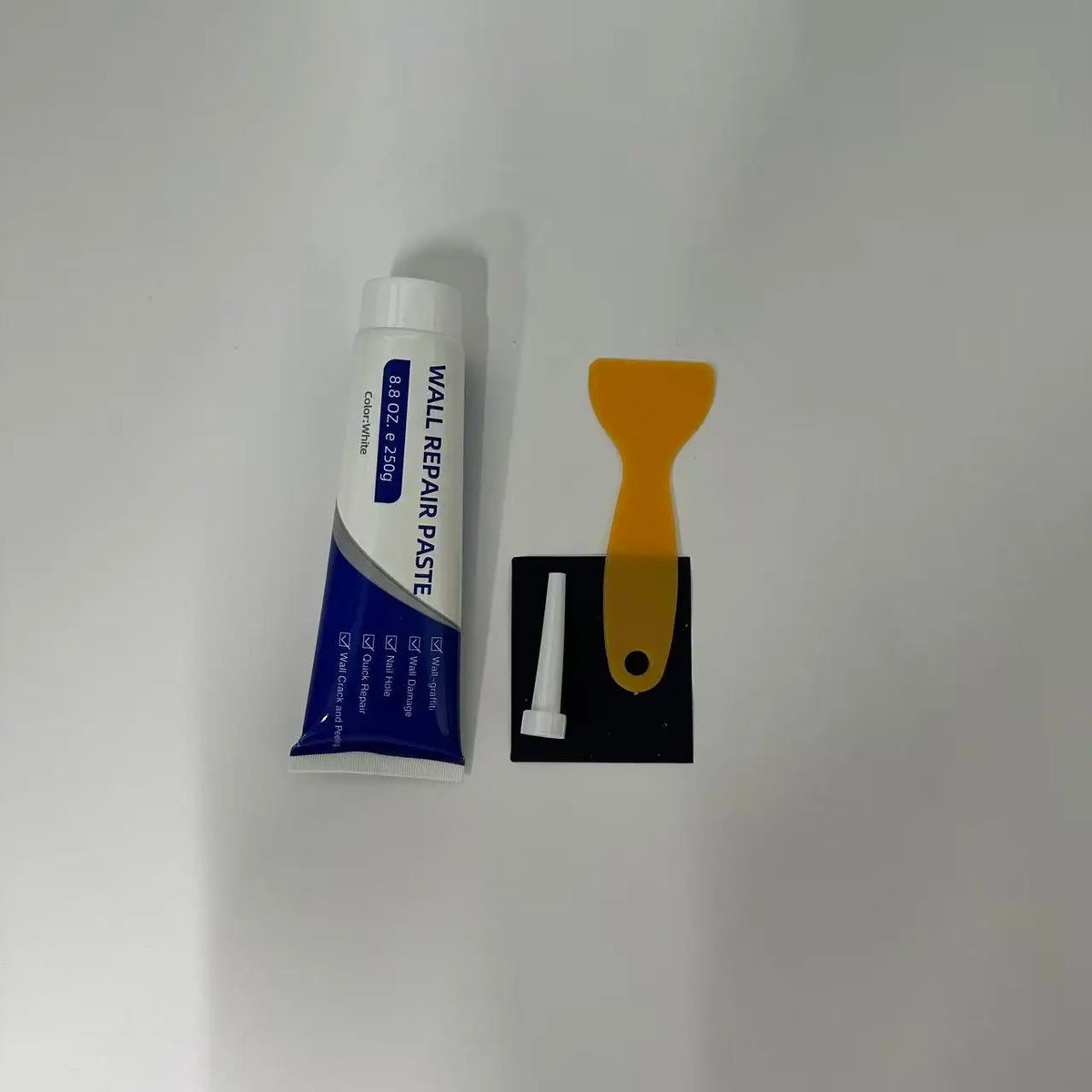 Tube of white wall repair paste with an orange scraper and a white piece of sandpaper.