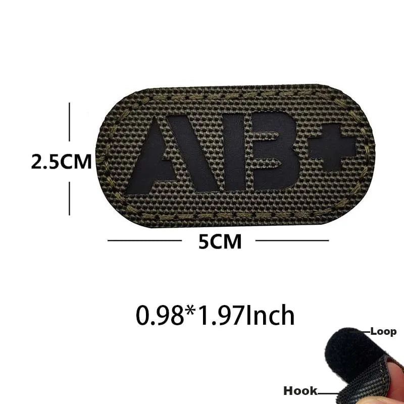 A black glow-in-the-dark blood type tactical patch with hook and loop backing shown next to a measuring scale.