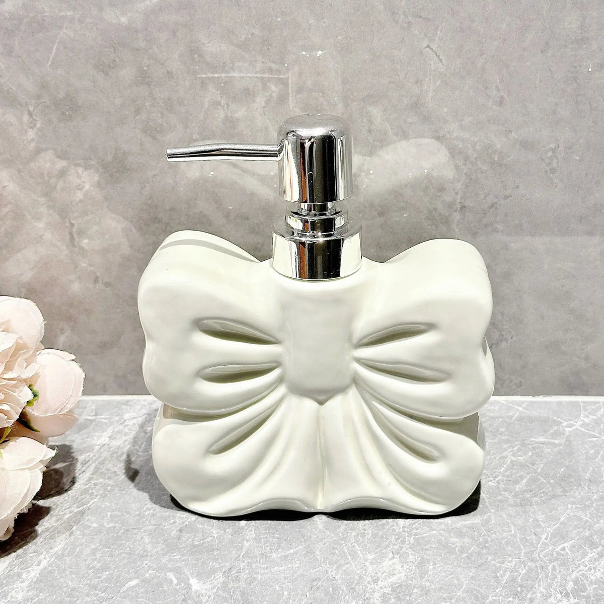 A white ceramic pump dispenser with a silver pump mechanism sits on a gray surface.