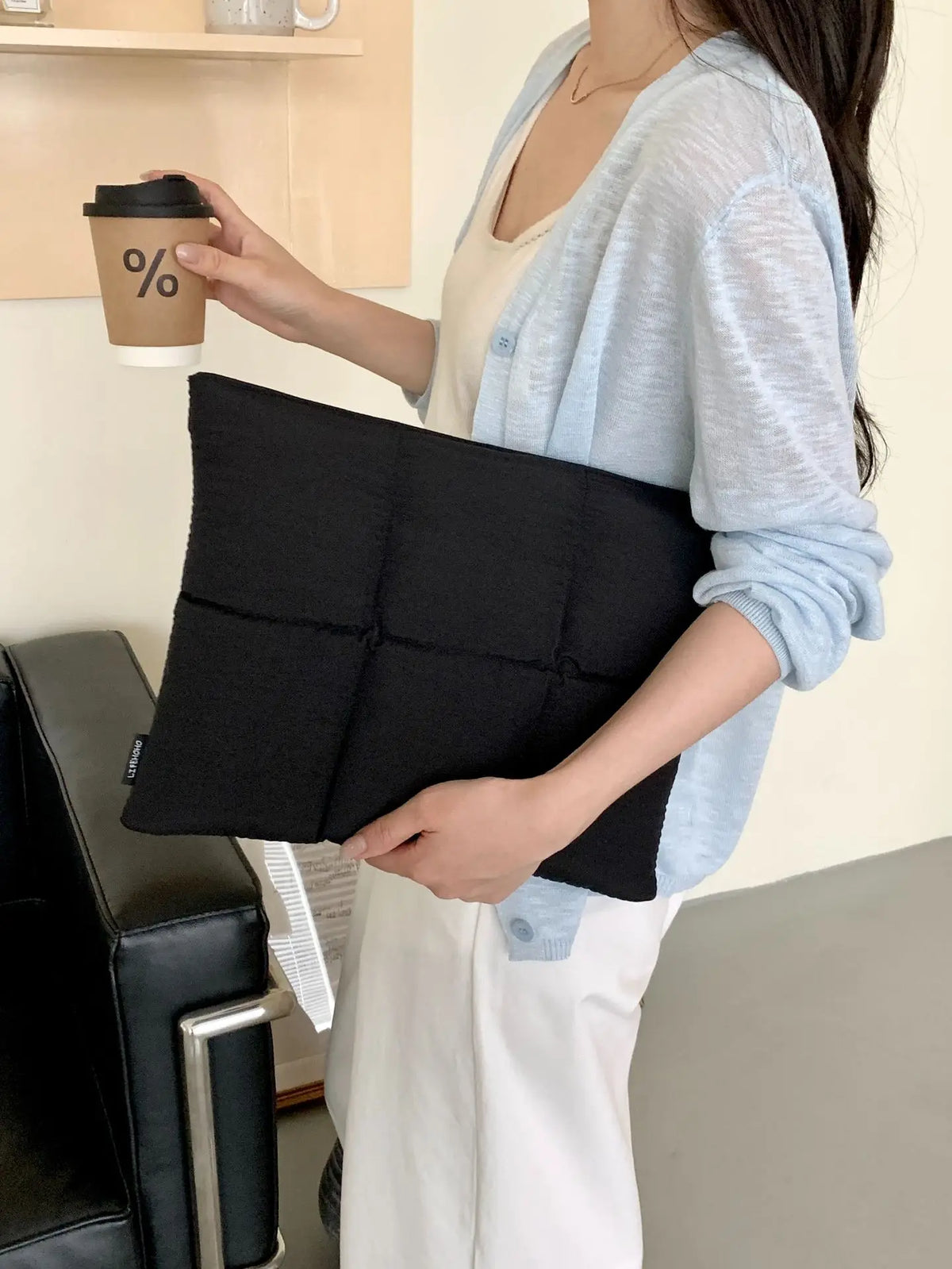 Person hält schwarze gesteppte Laptoptasche mit Reißverschluss.