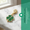 Gold-toned four-leaf clover charm on a white marble surface with green background text.
