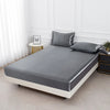 Graues Satin-Bettwäsche-Set mit zwei Kissen auf einem modernen Bett in einem hellen Raum.