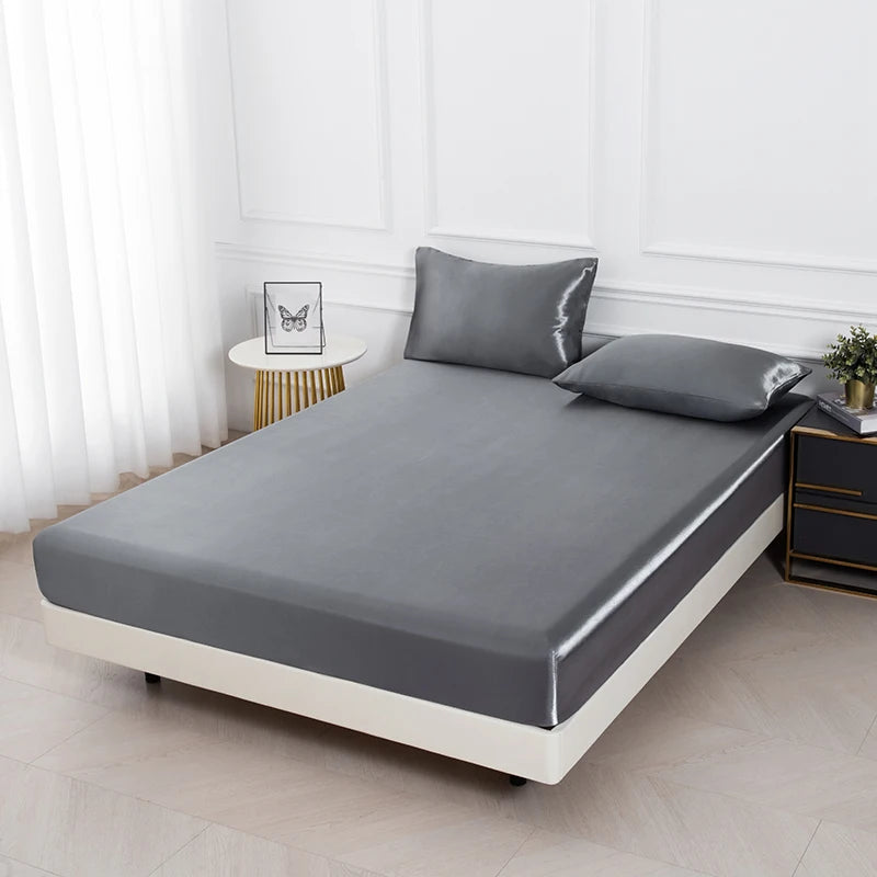 Graues Satin-Bettwäsche-Set mit zwei Kissen auf einem modernen Bett in einem hellen Raum.