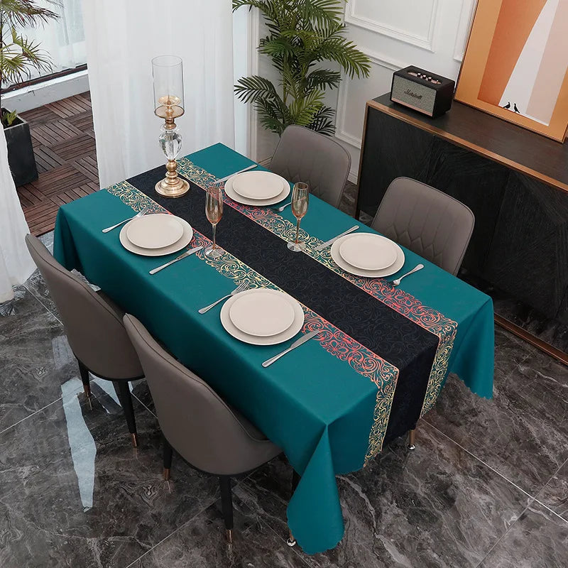 A long dining table set with a teal tablecloth, gold accents, and gray chairs in a modern interior.