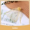 A clear organza drawstring gift bag with dried greenery is displayed on a wooden surface.