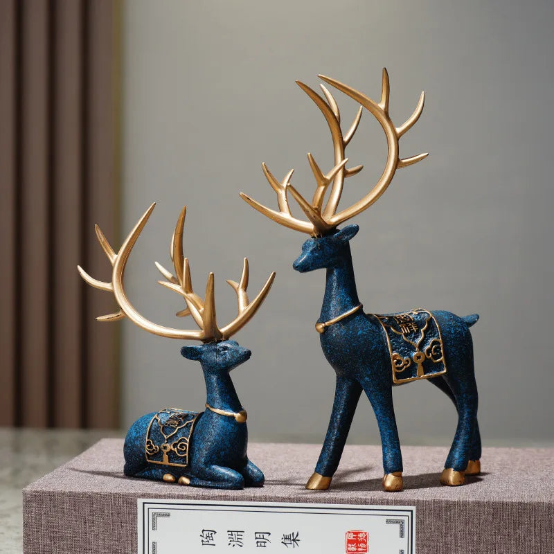 A set of two blue resin deer figurines with gold accents displayed on a light gray surface.