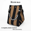 A hand bag featuring black and tan vertical stripes with a black and white patterned strap.