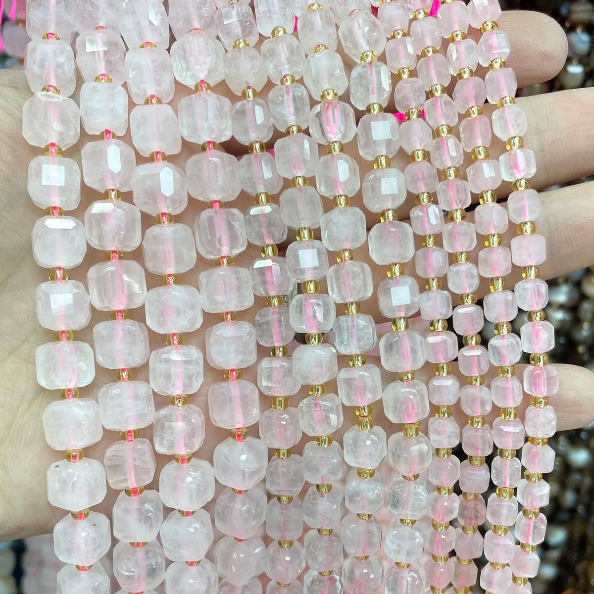 A hand holds a string of square faceted pink quartz beads for jewelry making