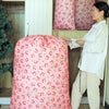 A pink drawstring laundry bag with a floral pattern is displayed next to a woman in a white shirt.