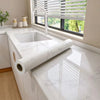 A white marble peel-and-stick film is shown on a kitchen countertop with a sink and window.
