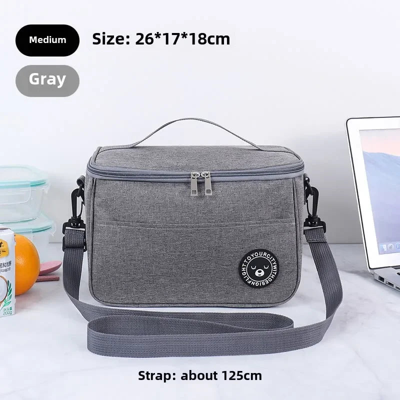 A gray insulated lunch bag with a strap is shown on a white surface.