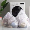 A white washing machine is shown with four mesh laundry bags in front of it.