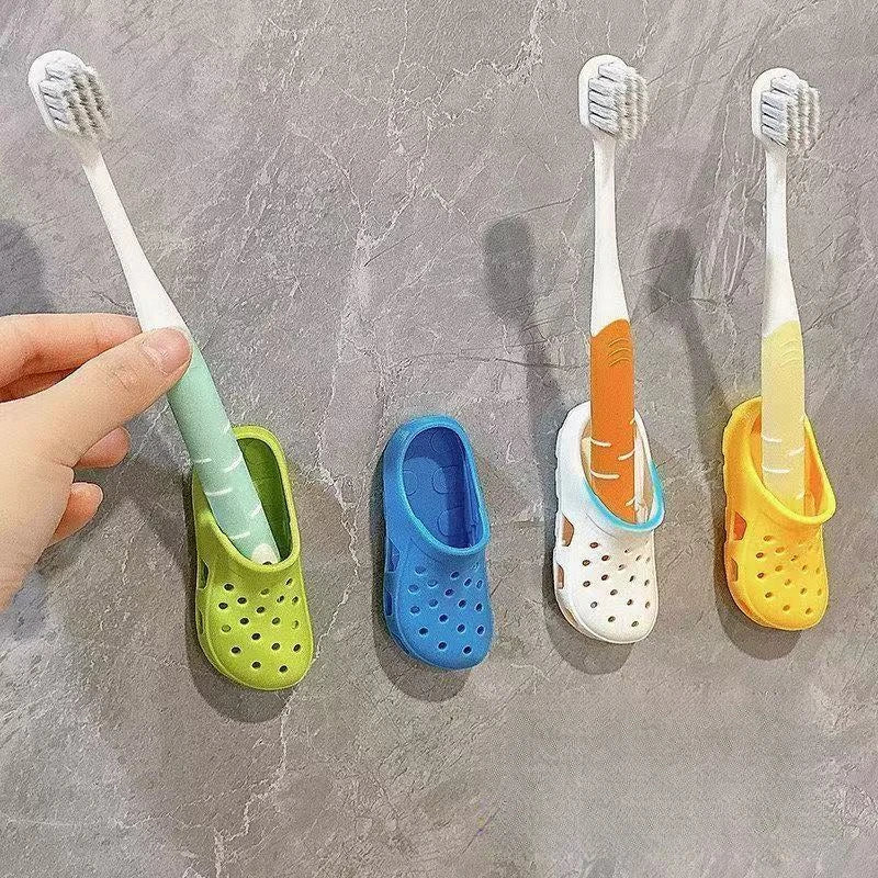 A hand holds a white toothbrush and places it into a colorful, wall-mounted holder with drainage holes.