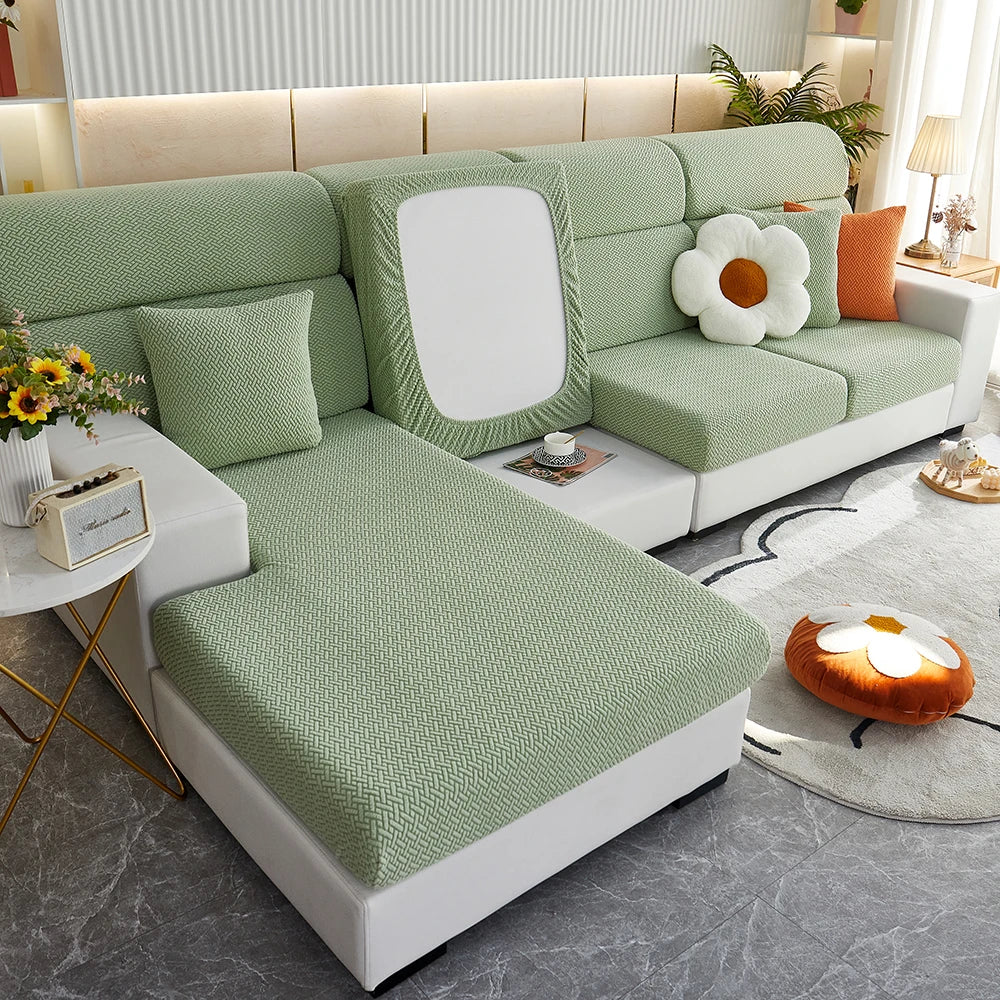 A light green elegant jacquard sofa slipcover with a white backrest and decorative pillows in a modern living room setting.