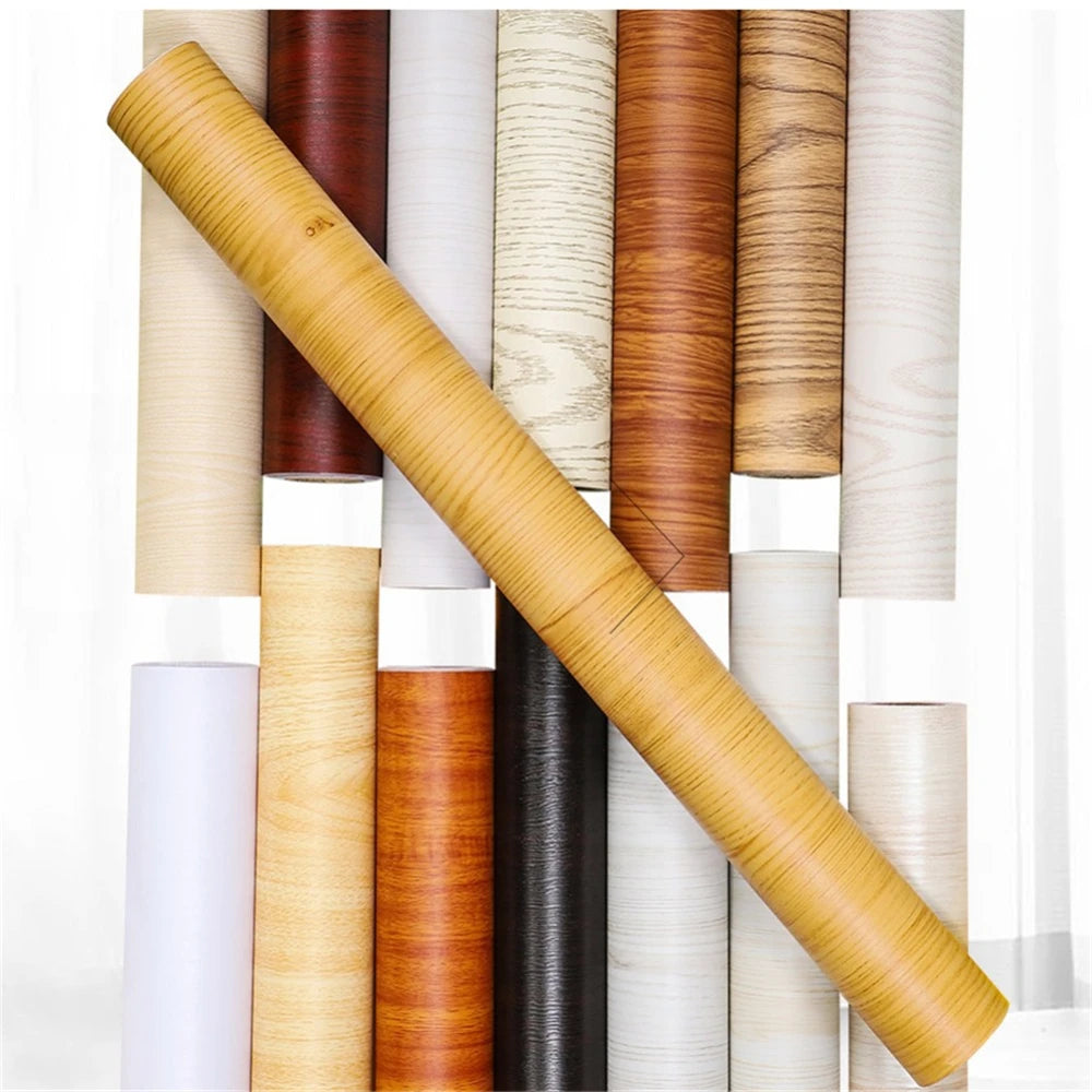 A close-up view of various rolls of self-adhesive wood grain waterproof wallpaper in different natural wood tones.