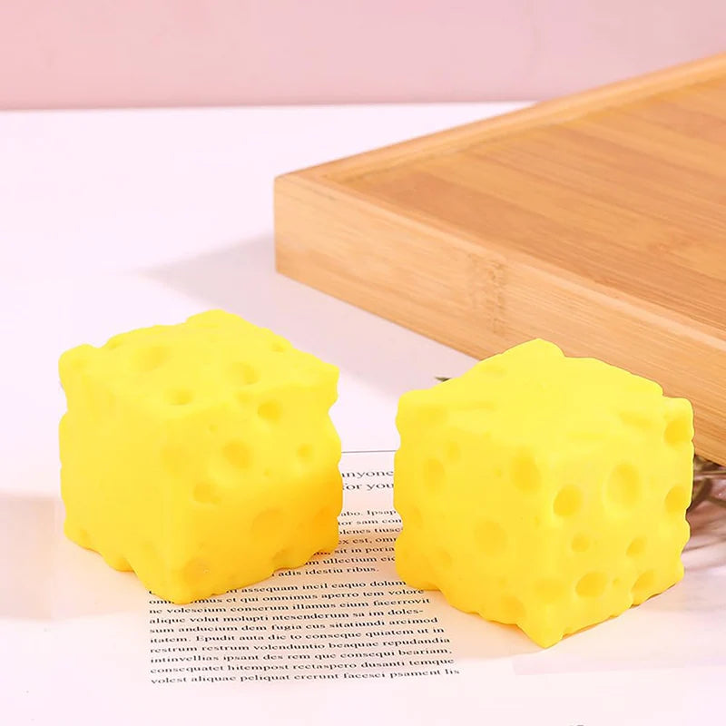 Jouet anti-stress en forme de fromage jaune vif posé sur une planche à découper en bois.