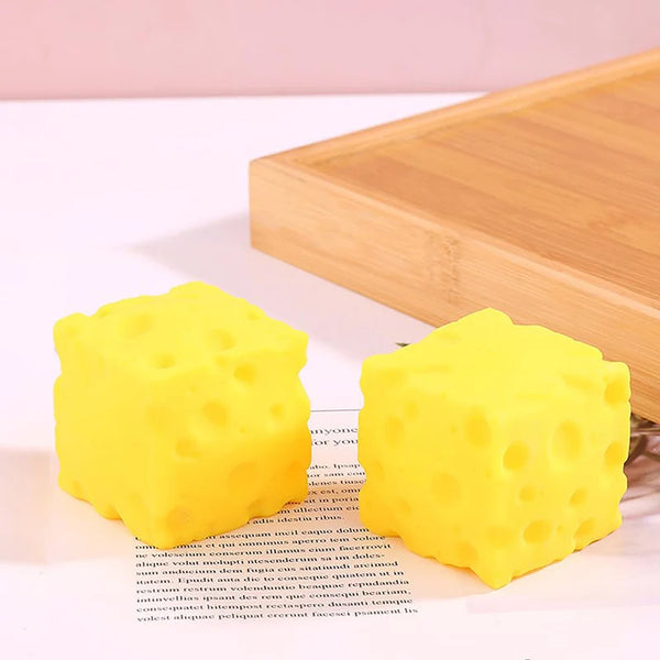 Jouet anti-stress en forme de fromage jaune vif posé sur une planche à découper en bois.