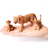 Three realistic tiger figurines of different sizes are displayed on a person's hand.