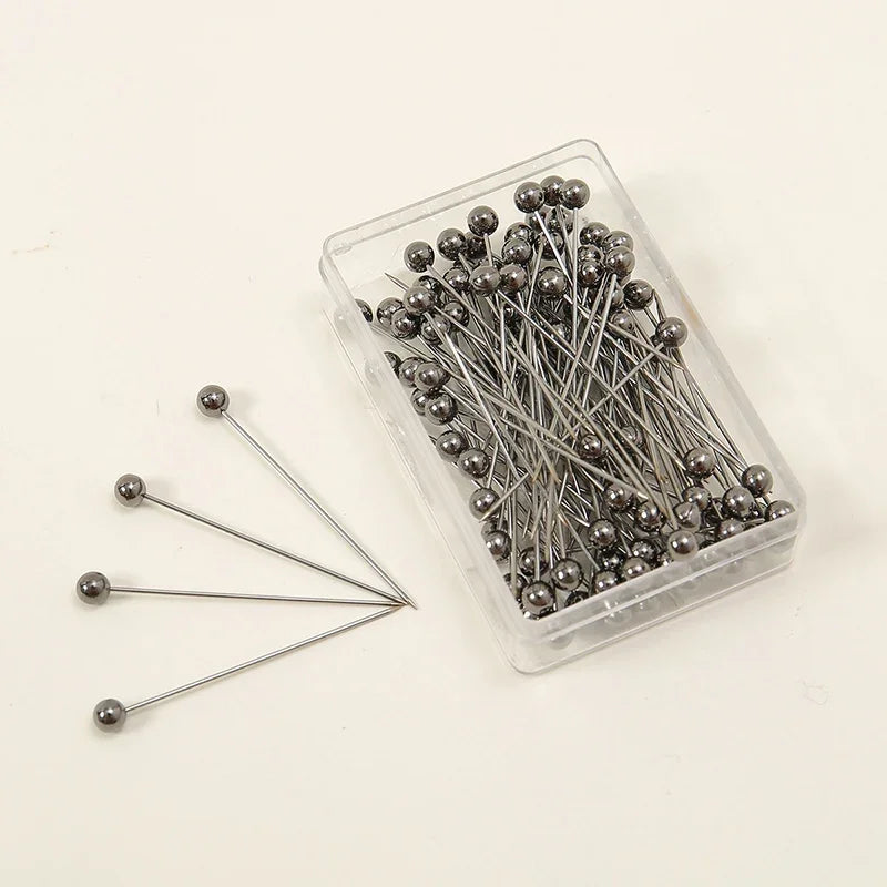 A clear plastic container filled with 100 precision metal quilting pins for sewing and crafting.
