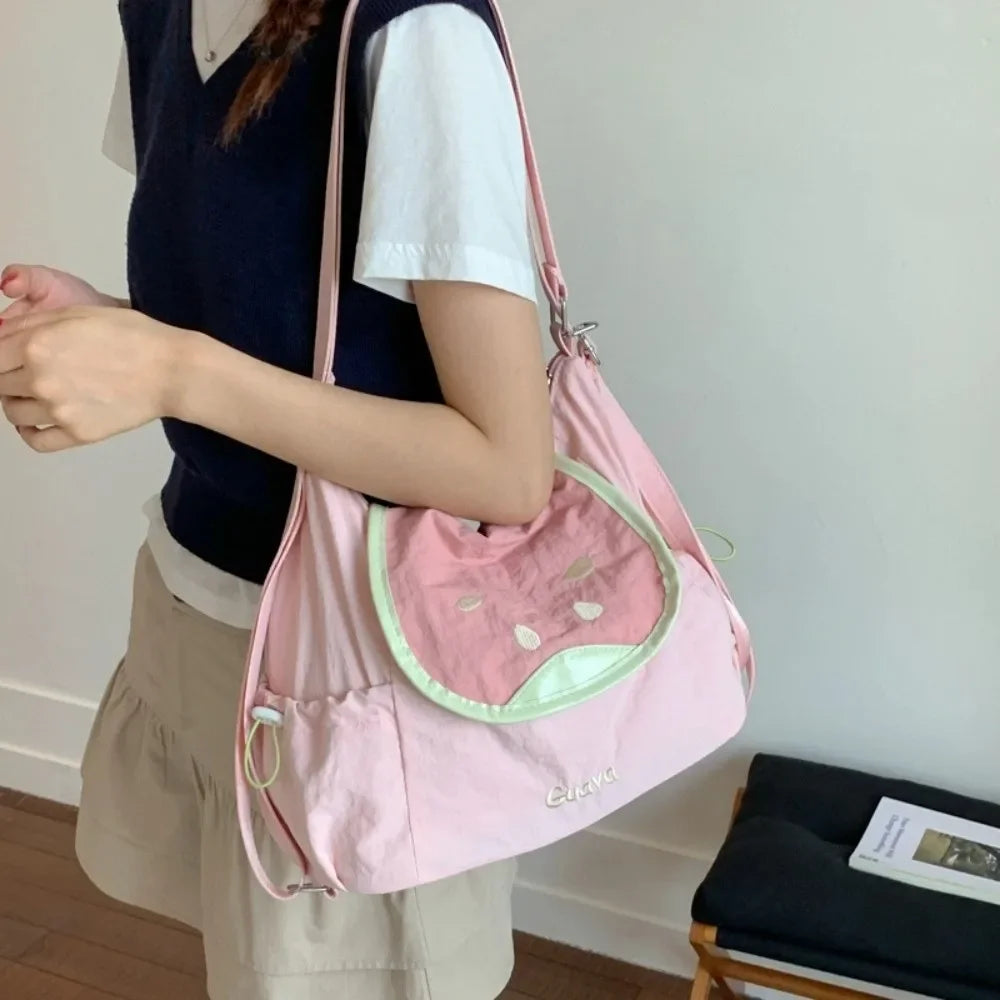 A person is holding a pink nylon messenger bag with a light green accent against a white background.