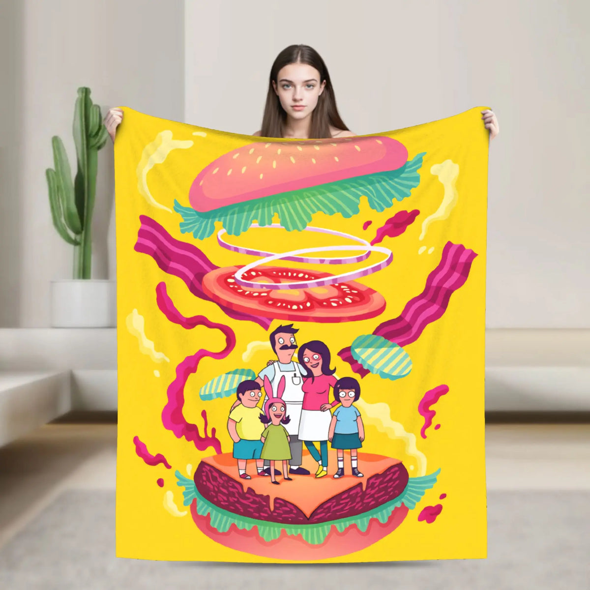A yellow throw blanket featuring a playful cartoon illustration of a hamburger and a family standing on the bun.