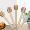 A set of natural wood honey dipper sticks with a golden piece of honey on a wooden surface.