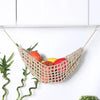 Macrame hanging fruit hammock filled with various colorful fruits suspended against a white background.
