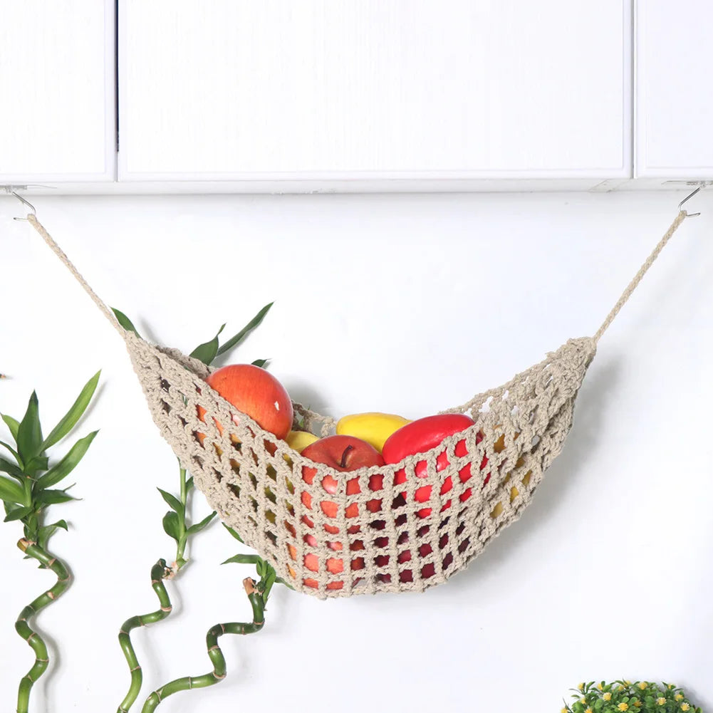 Macrame hanging fruit hammock filled with various colorful fruits suspended against a white background.