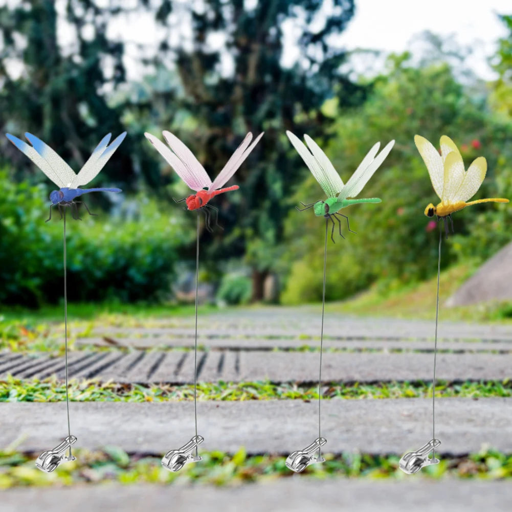 Several lifelike dragonfly clips with iridescent wings are displayed on thin wires in a garden setting.