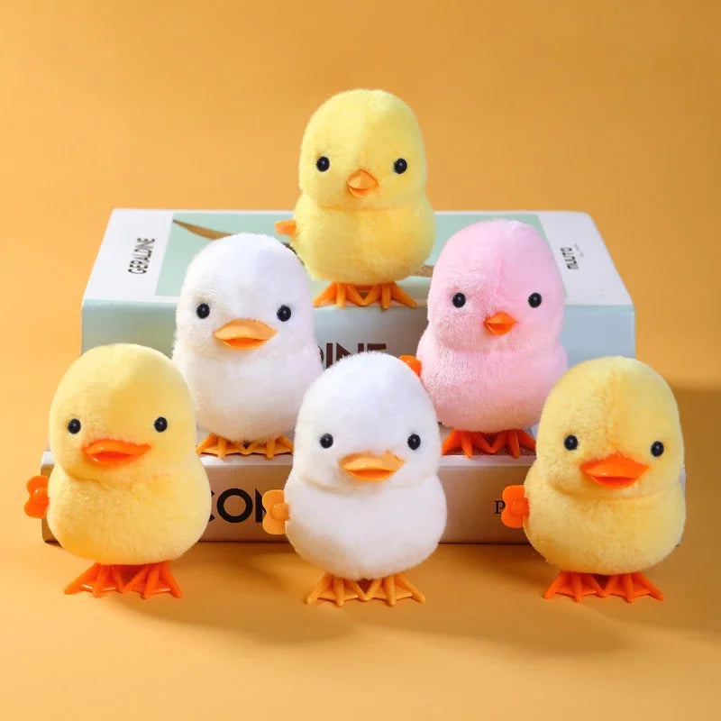 A set of four yellow and pink wind-up walking chicken toys displayed on a light box.