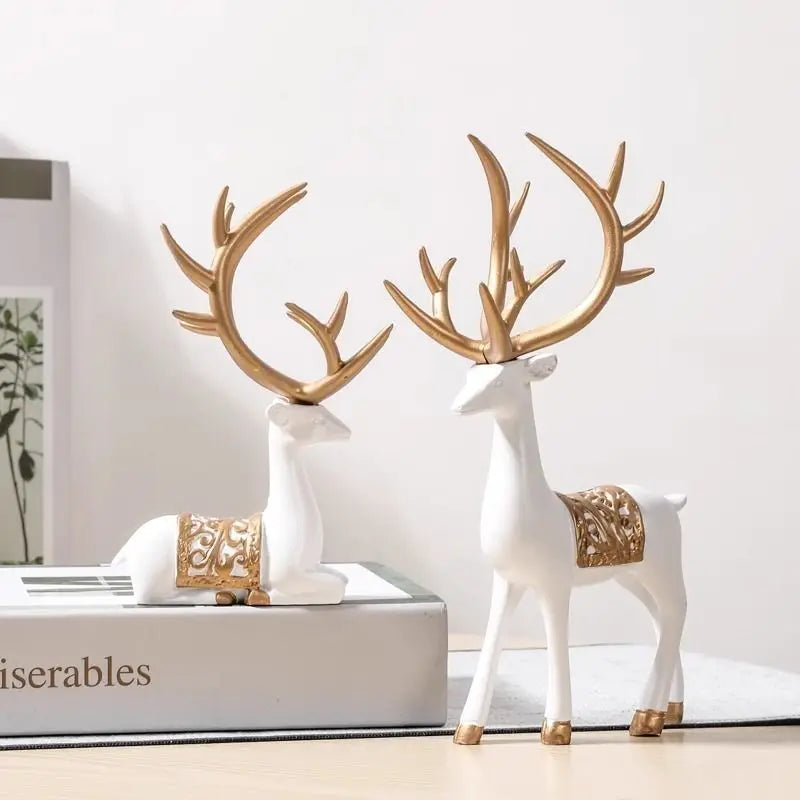 A set of two white resin deer figurines with gold antlers displayed on a white box.