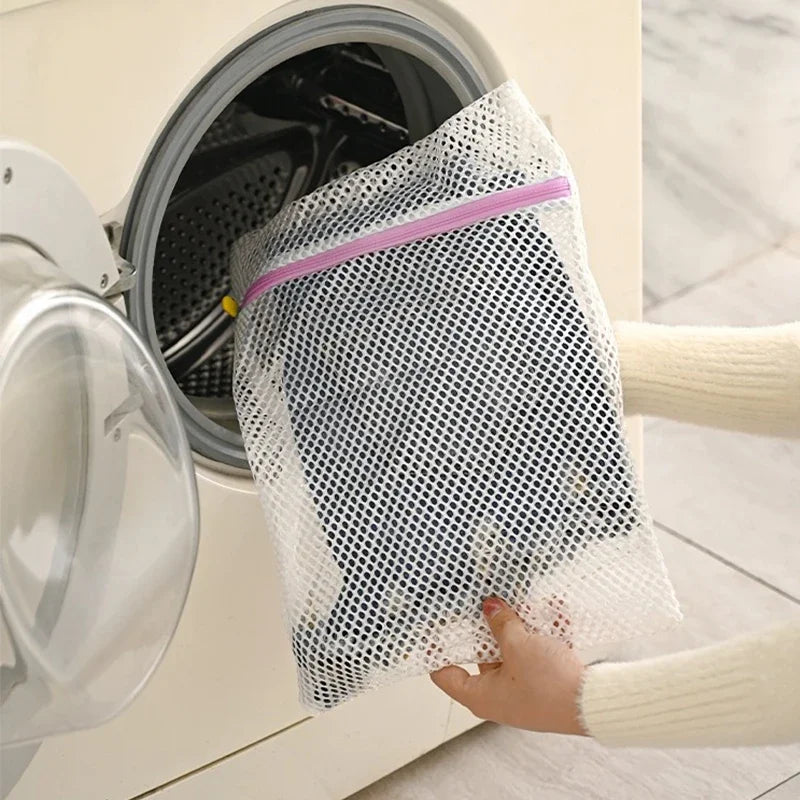 A hand is placing a mesh laundry bag with a pink strap into the drum of a white washing machine.