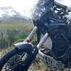 Close-up of a black motocross motorcycle fork with custom stickers and components in an outdoor setting.