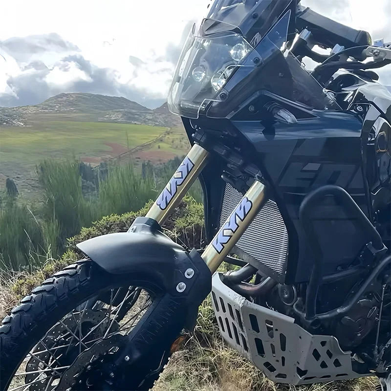 Close-up of a black motocross motorcycle fork with custom stickers and components in an outdoor setting.
