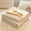 A stack of cream and yellow lace-trimmed breathable summer duvets resting on a quilted bedspread.