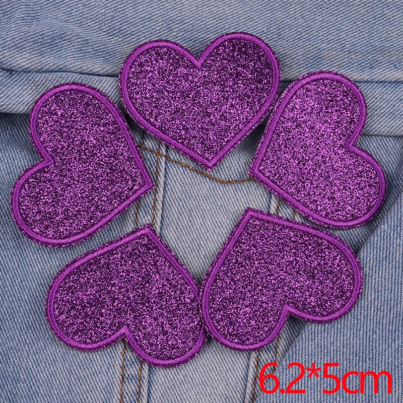 A set of five purple glitter heart iron-on embroidered patches on a denim fabric background.