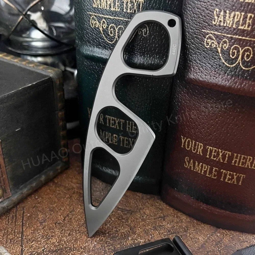 A silver compact stainless steel neck knife with a distinctive shape is shown resting on a wooden surface.