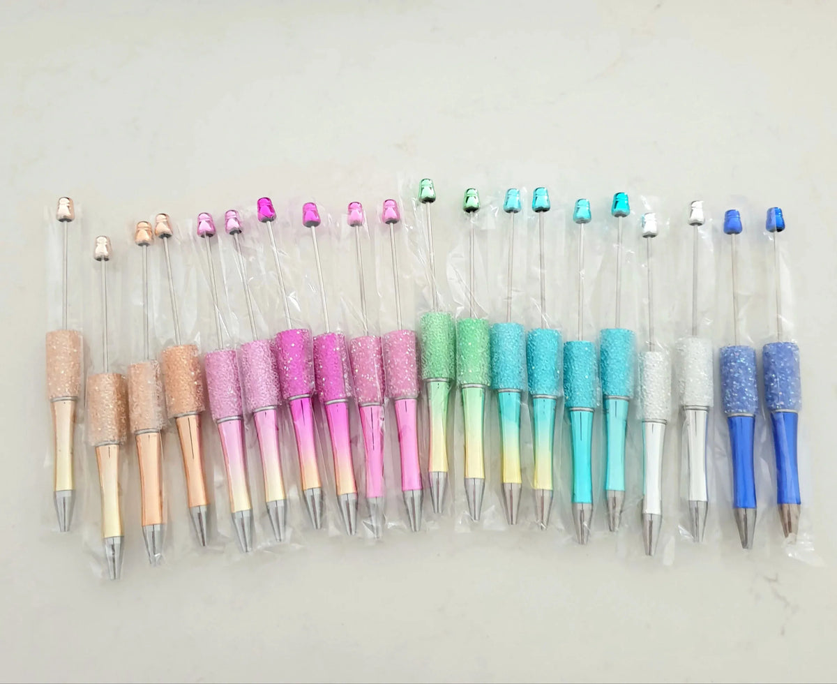 Une collection de trente stylos-plumes à bille perlés de différentes couleurs et finitions, disposés en rangée.