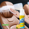 A hand is applying a white foam cleaner to brown car upholstery inside a vehicle.