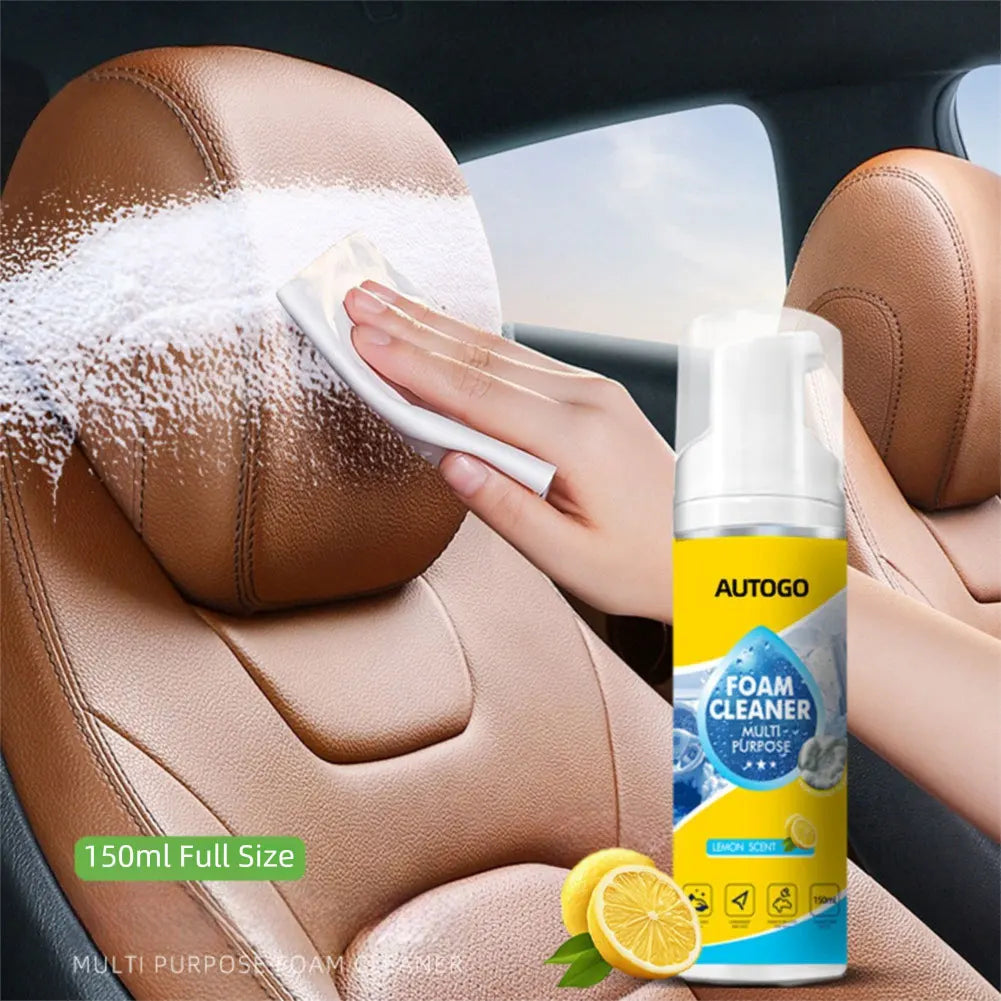 A hand is applying a white foam cleaner to brown car upholstery inside a vehicle.