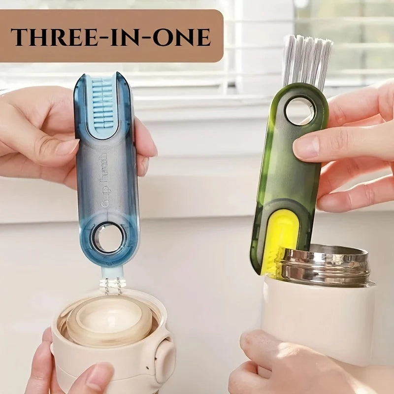 A hand holds a three-in-one cup and bottle cleaning brush set with a green handle and yellow bristles.