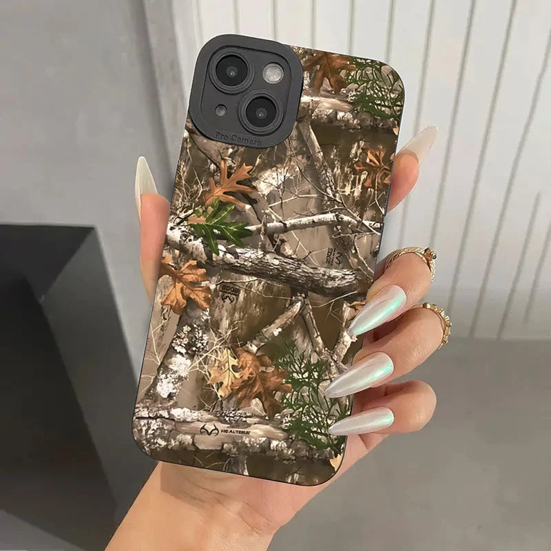 A hand holds a phone with a forest camouflage silicone case featuring tree branches and autumn leaves.