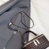 A dark brown woven PU leather crossbody bag with silver hardware resting on a gray blazer.