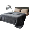 A silver water dispenser is pouring water onto a dark gray flannel blanket on a bed.