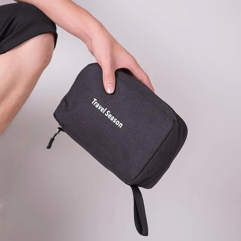 A hand is holding a black hanging travel toiletry bag with the text Travel Season on it.