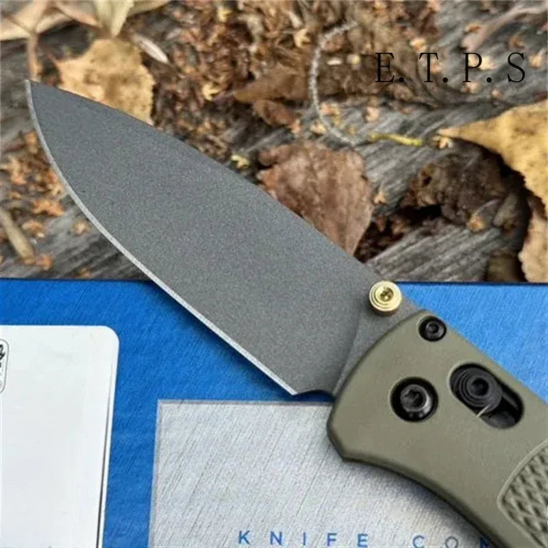 A gray CPM-20CV folding pocket knife with a drop point blade resting on a blue surface.