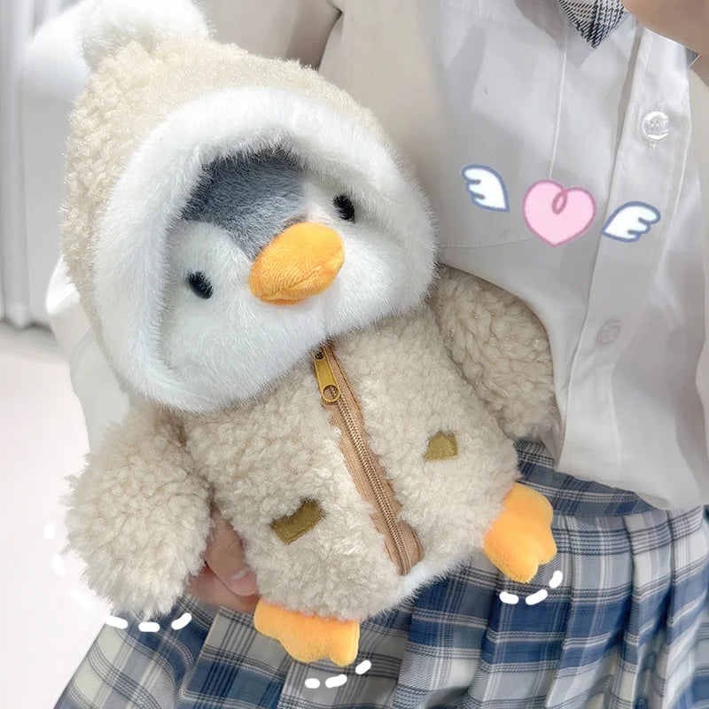 A fluffy white penguin plush toy wearing a hood and featuring orange feet, held against a plaid skirt.