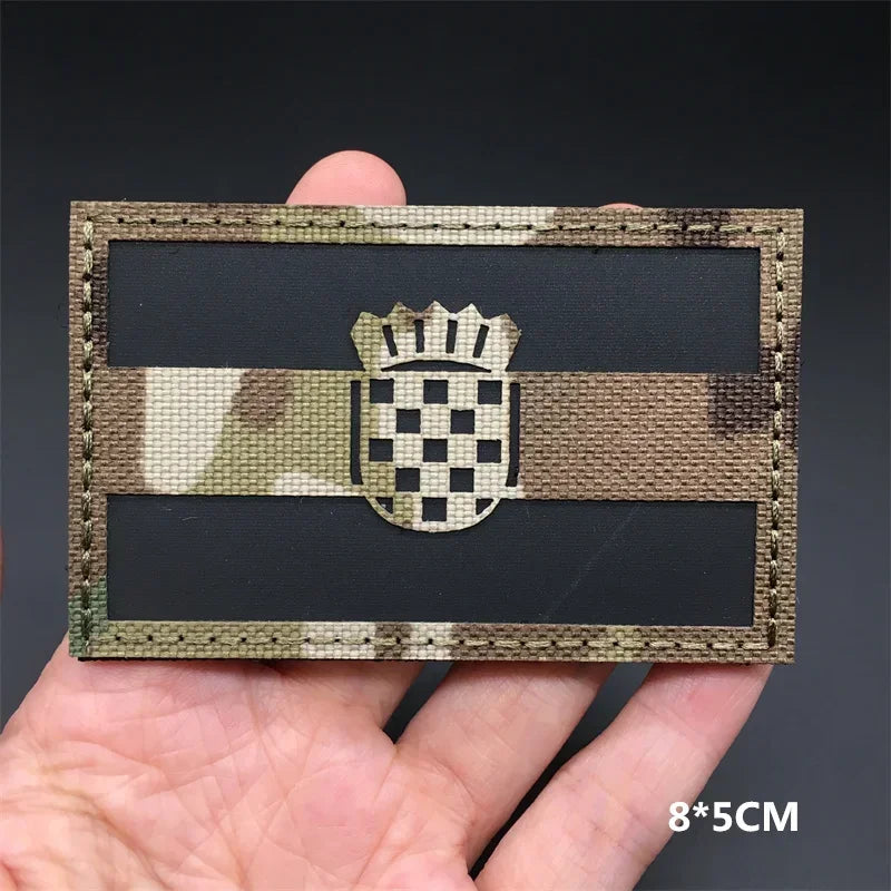 A rectangular tactical patch featuring a camouflage pattern and a national flag design with hook-and-loop backing.